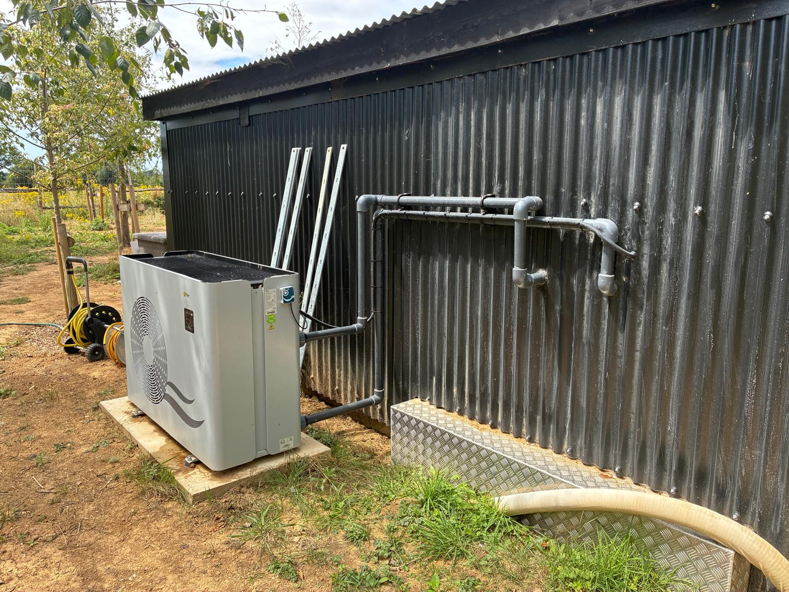 Swimming pool heat pump connected to new pipework beside a garden shed