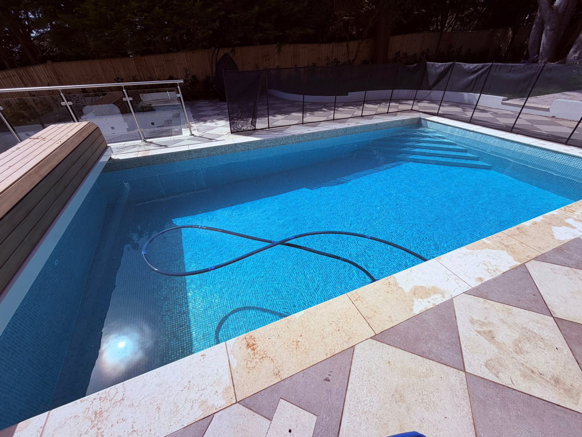 Blue-tiled swimming pool being vacuumed during a routine pool service