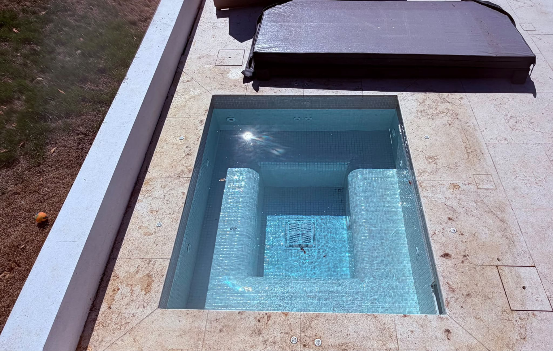Newly installed tiled spa with cover beside stone paving