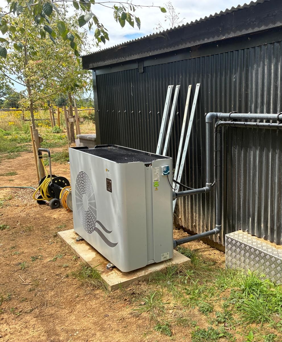 Pool heat pump on a paving slab beside a plant room, with trees behind